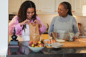 Happy african mother and daughter having fun cooking together inside kitchen at home - Family, love...
