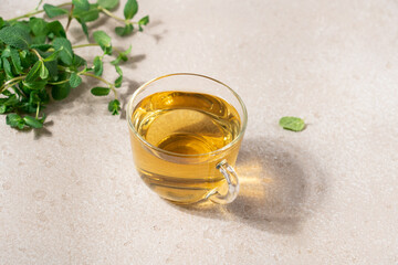 Fresh hot tea from green mint leaves in glass mug on beige background. Herbal healthy drink in cup