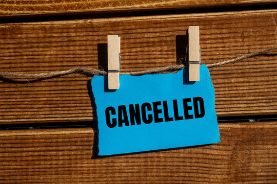 Cancelled message written on ripped blue torn paper piece with wooden background. Conceptual cancelled symbol. Copy space.