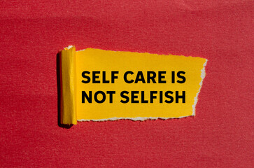Self care is not selfish message written on ripped torn yellow paper on red background. Conceptual self care is not selfish symbol. Copy space.