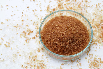 Natural cane sugar in a petri dish, with sugar of more colors and different crystal size around. Health, nutrition or scientific concept