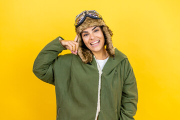 Young beautiful aviator woman wearing vintage pilot helmet with glasses and jacket over yellow background smiling and thinking with her fingers on her head that she has an idea.