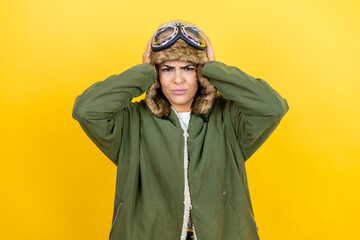Young beautiful aviator woman wearing vintage pilot helmet with glasses and jacket over yellow background thinking looking tired and bored with hands on head