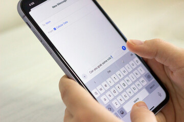 Hands holding a smartphone with a message 'Can you grab some milk?', (day mode), isolated neutral background
