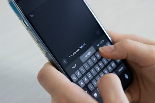 Human hands holding a smartphone and typing a message with predictive text (are you free tonight?)