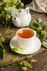 Healing herbal tea with lime blossom in a mug on a dark wooden table with flowers