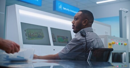 African American Security Officer Controls Luggage Scanning on Computer Monitors Using Modern...