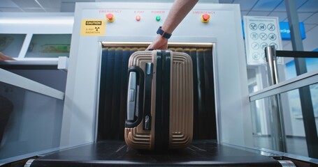 Security Check in Airport Terminal: Passenger Places Suitcase on Conveyor Belt for Baggage...