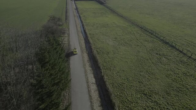 Une 4L jaune embl&eacute;matique traverse des champs le long d'un route sinueuse, film&eacute;e &agrave; partir d'un drone