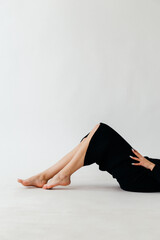 A confident young woman in a black ribbed midi dress poses gracefully against a minimalistic white...