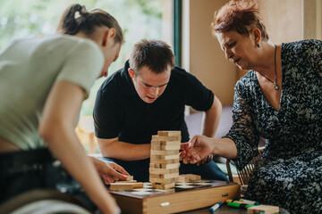 A boy with Down syndrome, a girl in a wheelchair, and an elderly woman engage in a fun building blocks game, promoting inclusion and friendship.