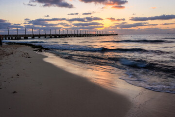 A beach with a pier and the sun setting in the background