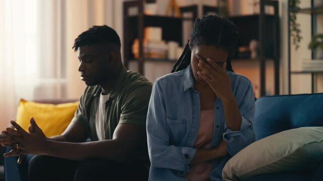 Stressed couple sits apart on sofa, dealing with unresolved relationship issues