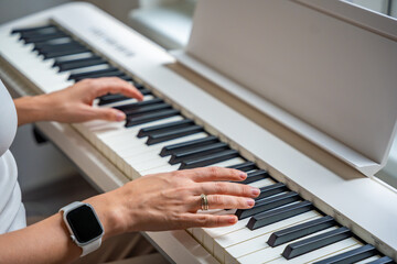 Fototapeta premium Closeup woman's hand playing piano. Concept of home lesson of music: learning music enhances motor skills, hearing, and intelligence, fostering creativity