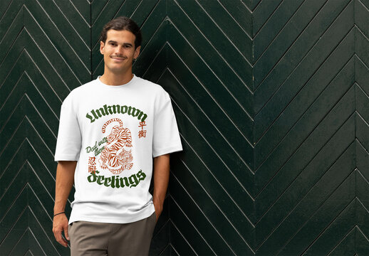 A man leans casually against a green herringbone wall in a customizable short sleeve t-shirt, showing its style.