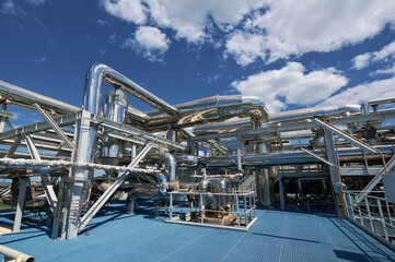 Fototapeta premium Pipelines and machinery in a chemical plant under a bright blue sky with scattered clouds during daylight operations