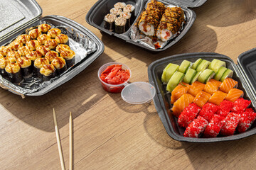 Three boxes of sushi sets on wooden table. Asian food delivery at home. Wooden chopsticks and pickled ginger