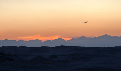 airplane in the sky at sunset time above the mountains