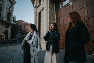 Three businesswomen standing outside a large building in an urban setting, engaged in lively...