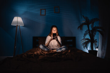 Teenage girl using smart phone in bed at night, young gamer playing games or watching videos online...