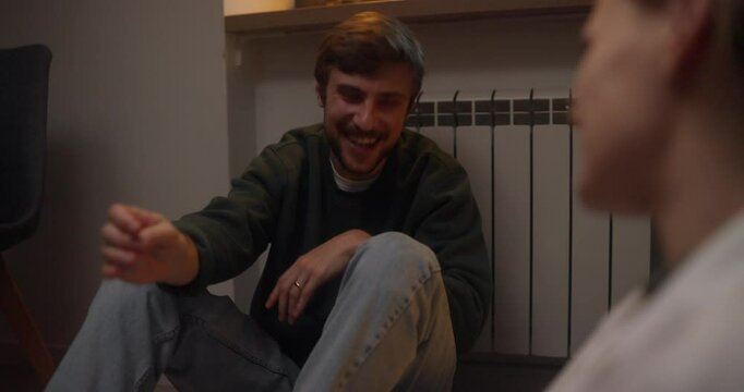 Happy blond guy with a mustache in a green jacket holds hands together with his girlfriend and communicates during a happy romantic moment at home in the evening