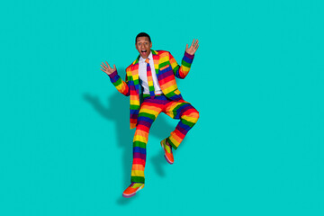 Charismatic Man Jumps in Stylish Rainbow Suit on Turquoise Background Expressing Joy