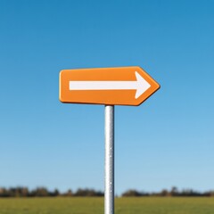 orange directional arrow sign against a clear blue sky pointing to the right, with a blurred field in the background.