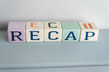 Colorful blocks spell out the word "RECAP" on a light blue surface, showcasing a playful and educational theme.