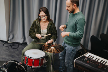 A music teacher guiding a student on a drum kit within a music rehearsal studio.