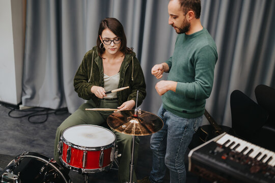 A music teacher guiding a student on a drum kit within a music rehearsal studio.