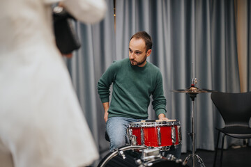 A drummer adjusts his red drum set while preparing for a music rehearsal session.