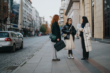 Three stylish women interact on a city sidewalk with modern buildings in the background.