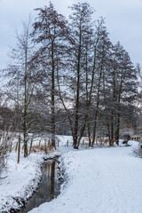 Idyllic view over the frozen creek, bare trees and meadows covered with snow in the Baudouin park