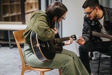 A musician guides another in improving their skills on an acoustic guitar during practice. Both are...