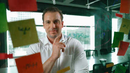Smart businessman thinking about start up project in front of glass board. Smiling male project...