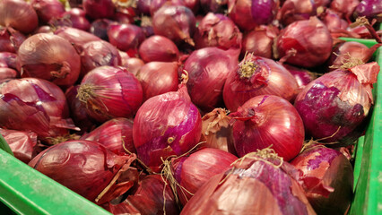 Red onion close-up in supermarket. Lots of red onions in plastic green box on market stall. Onions...