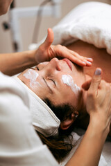 Professional cosmetician applying beauty mask on female client's face. Middle aged woman receiving skincare treatment in beauty spa or salon.
