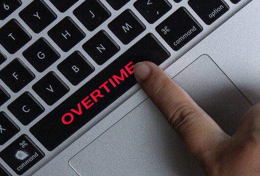 Close-up of Finger Pressing Laptop Key with Red Overtime Text for Workplace Productivity Concept