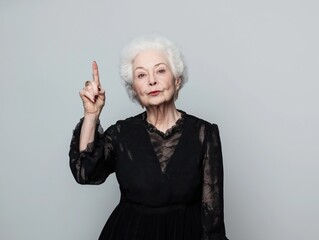 Elderly woman making a point while wearing elegant black dress against neutral background