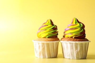 Tasty cupcakes with colorful cream on yellow background, closeup. Space for text