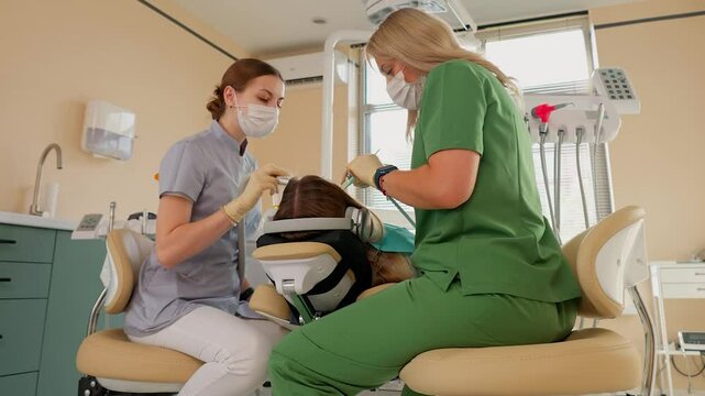 Blonde Woman Dentist with Assistant Treat Teeth of Female Patient with Special Instrument. Treatment of Caries and Plaque in Dental Clinic. Concept of Medicine and Healthcare. Slow Motion.