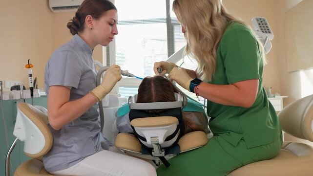 Blonde Woman Dentist with Assistant Treat Teeth of Female Patient with Special Instrument. Treatment of Caries and Plaque in Dental Clinic. Concept of Medicine and Healthcare. Slow Motion.