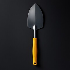 a small stainless steel trowel with a yellow handle on a black background