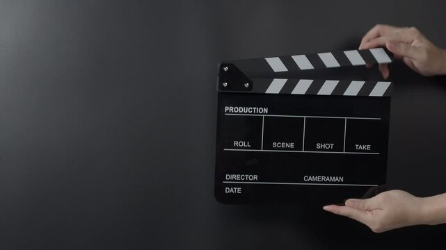 A classic film clapperboard or film slate being held and hit against a dark background. Symbolizes filmmaking video production movie filming and creative storytelling in the entertainment industry.