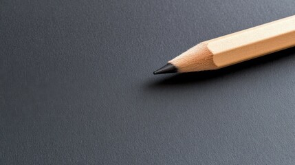 A single pencil lays poised on a smooth dark surface, highlighting simplicity and readiness for creativity or writing.