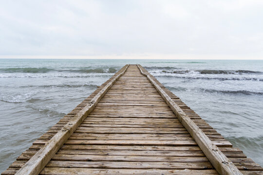 Fototapeta Wooden pier leading to the Adriatic Sea on a cloudy autumn beach in Italy