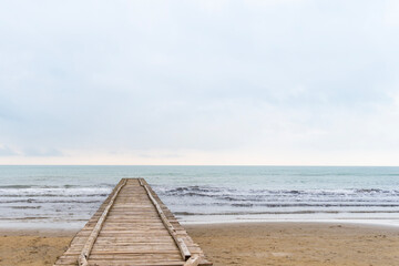 Obraz premium Wooden pier leading to the Adriatic Sea on a cloudy autumn beach in Italy