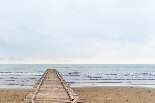 Wooden pier leading to the Adriatic Sea on a cloudy autumn beach in Italy