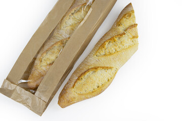 Two freshly baked baguettes, one wrapped in brown paper bag, Artisan French baguettes with crispy crusts in paper packaging. Isolated on a white background. Closeup. With clipping path..