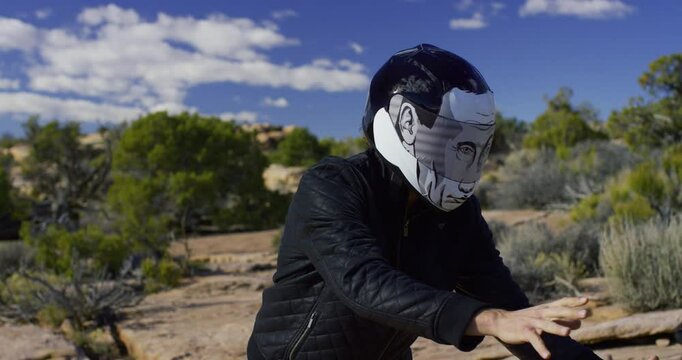 Biker gang member in funny helmet putting on parachute backpacks in rocky desert, steady cam shot
